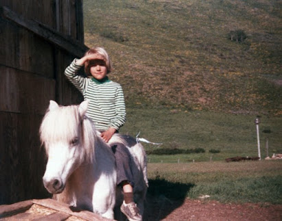A child riding a small white pony on a farm