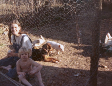 A woman and child sitting by a dog and farm animals.