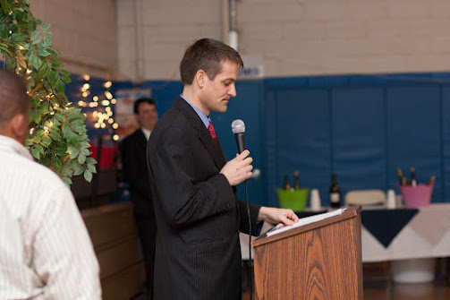 Sam speaking with a microphone to a room of people